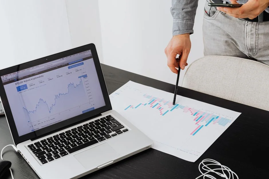 A modern workspace showing hands analyzing marketing data on a laptop and paper documents.